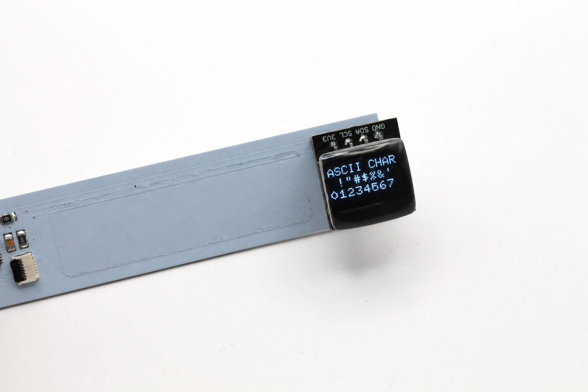 Tiny resin-lens OLED lit with white letters, symbols and numbers on an unlabeled pale blue demonstration board.